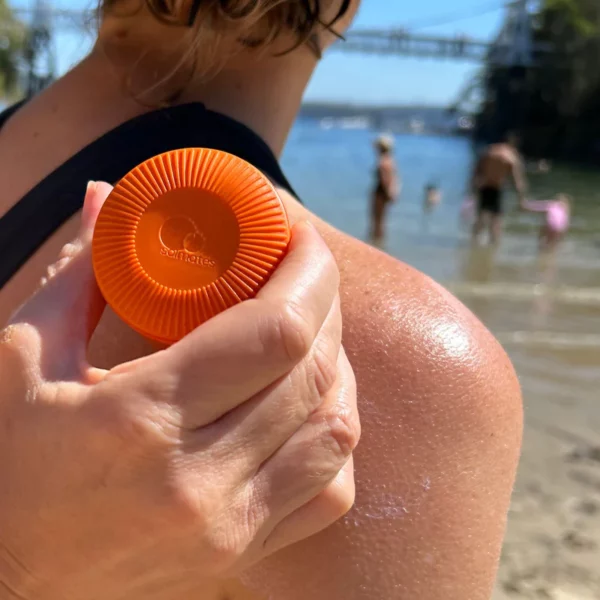 Orange Solmates Applicator being used on a woman back at the beach